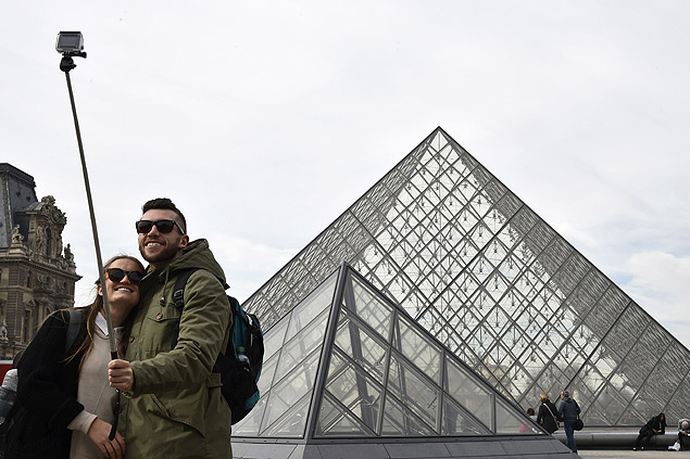 Turistas usam pau de selfie para tirar foto em frente a pirmide do Museu do Louvre, em Paris
